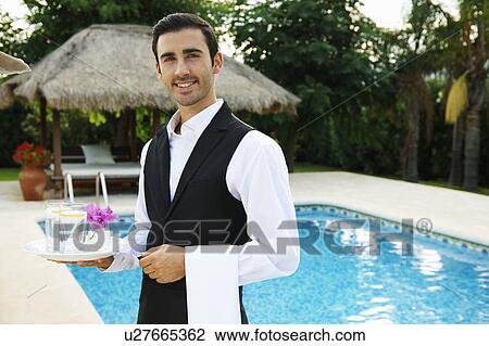 Stock Image - Hotel waiter holding tray by hotel pool. Fotosearch
