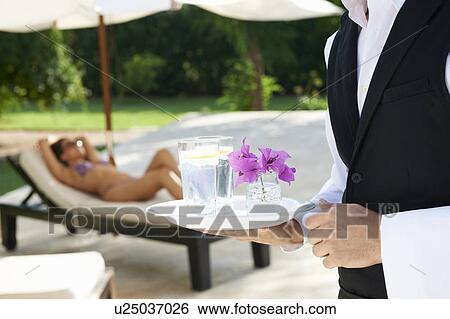 Stock Photograph - Hotel waiter holding tray by hotel pool. Fotosearch