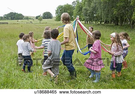 Stock Photography - Kids dancing round maypole in meadow. Fotosearch