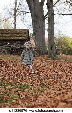 Stock Photograph - Little girl in leaf filled garden. Fotosearch