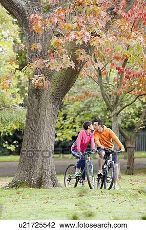Man and woman cycling in park kissing View Large Photo Image Stock Image - Man and woman cycling in park kissing. Fotosearch