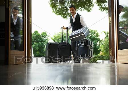 Man carrying suitcases into hotel View Large Photo Image Stock Photo - Man carrying suitcases into hotel. Fotosearch
