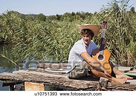 Stock Image - Man on jetty with guitar in the sun. Fotosearch