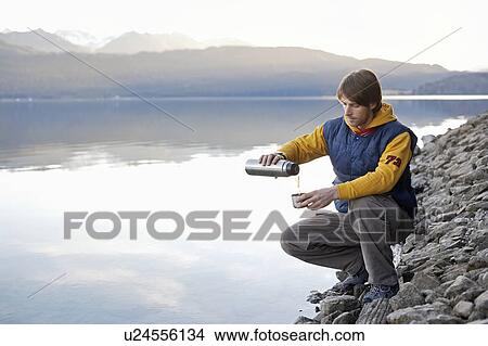 Man on lake in mountains with beverage View Large Photo Image Picture - Man on lake in mountains with beverage. Fotosearch