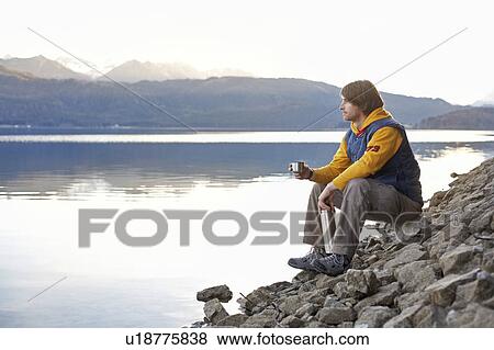 Man on lake in mountains with hot drink View Large Photo Image Stock Photo - Man on lake in mountains with hot drink. Fotosearch