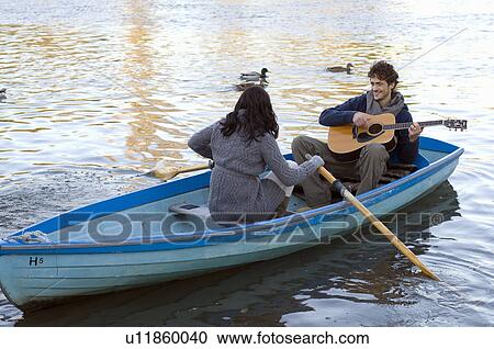Stock Image - Man playing guitar in row boat. Fotosearch