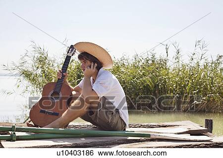 Stock Photograph - Man sitting on jetty speaking on phone. Fotosearch