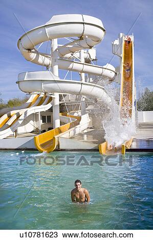 Stock Image - Man smiles in water at giant water slide. Fotosearch