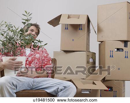 Stock Image - Man with a plant between packing boxes. Fotosearch