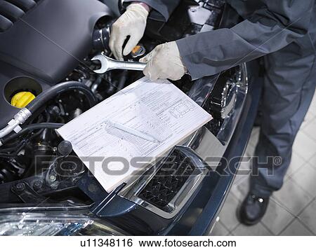 Stock Photograph - Mechanic checks list in car dealership. Fotosearch