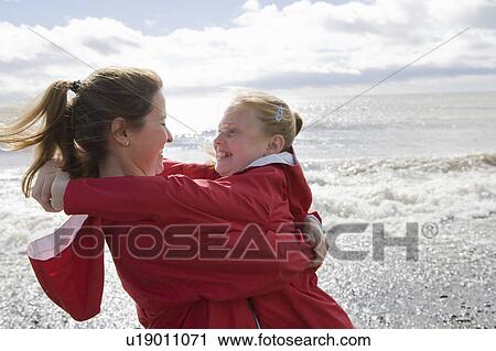 Stock Image - Mother and daughter hugging at beach. Fotosearch