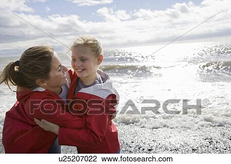 Stock Image - Mother and daughter hugging at beach. Fotosearch