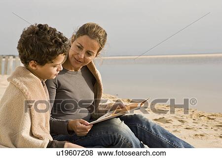 Stock Photo - Mother and son reading book at the beach. Fotosearch