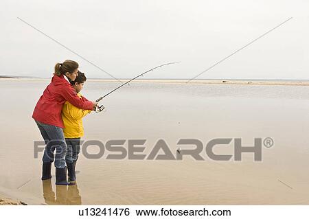 Stock Photograph - Mother teaching son to fish at beach. Fotosearch