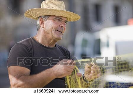 Stock Image - Old man preparing fishing net. Fotosearch