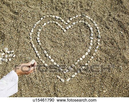 Stock Image -  Pebbles in heart shape on sand. Fotosearch