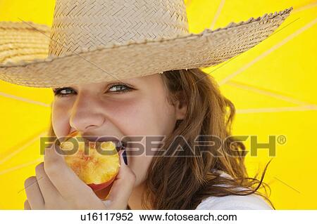 Stock Image - Pretty woman smiling and eating fruit. Fotosearch