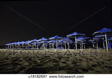 Stock Photo - Row of sun parasols at night. Fotosearch