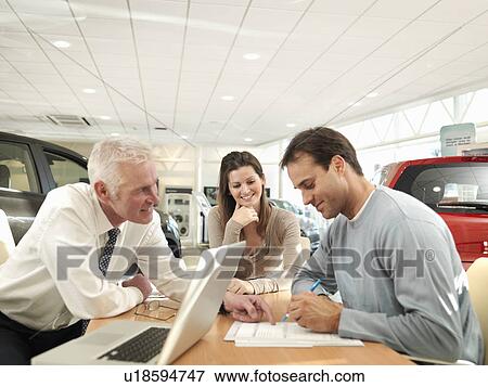 Stock Photo - Salesman and customers in car dealership. Fotosearch