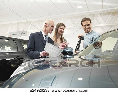 Stock Photo - Salesman and customers in car dealership. Fotosearch