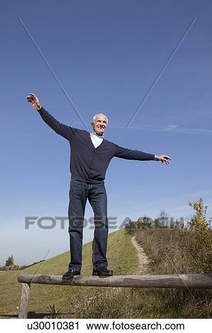 Stock Image - Senior man balancing along a wooden log. Fotosearch