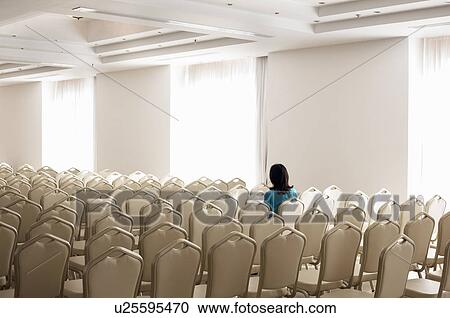 Stock Image - Solitary woman amongst empty chairs. Fotosearch