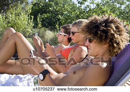 Teen group check phones laying in sun View Large Photo Image Stock Photo - Teen group check phones laying in sun. Fotosearch