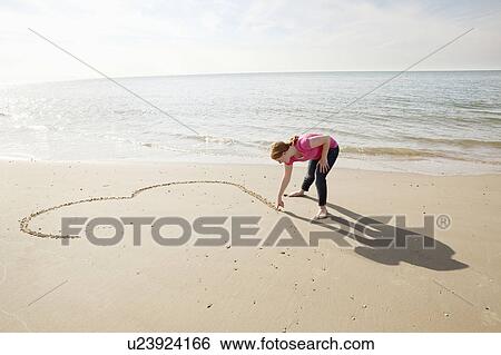 Stock Photograph - Teenager draws heart in sand on beach. Fotosearch