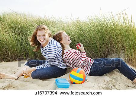 Picture - Teenagers laughing sitting in dunes. Fotosearch
