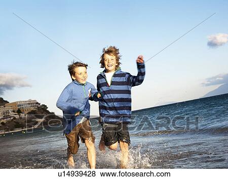 Stock Photo - Two boys running in surf on beach. Fotosearch