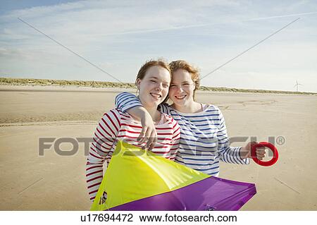 Stock Image - Two girls holding kite on beach. Fotosearch