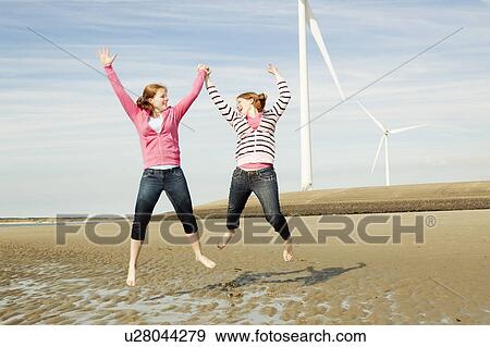 Two girls jumping on beach with turbines View Large Photo Image Stock Photo - Two girls jumping on beach with turbines. Fotosearch