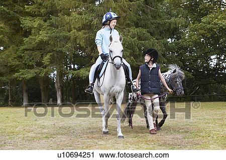 Stock Image - Two girls out riding ponies. Fotosearch