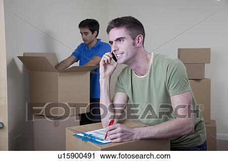 Stock Image - Two men unpacking boxes in apartment. Fotosearch