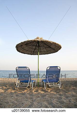Stock Photography - Two sunloungers and parasol on the beach. Fotosearch