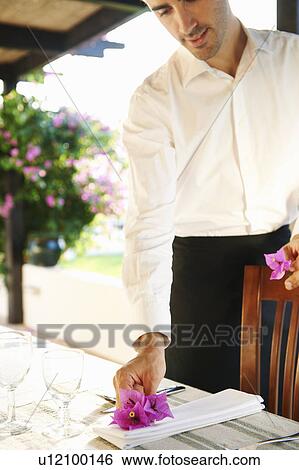 Stock Photograph - Waiter laying dinner table in hotel. Fotosearch