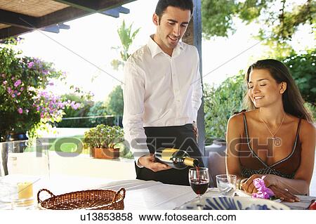 Stock Photo - Waiter pouring wine for woman at a table. Fotosearch