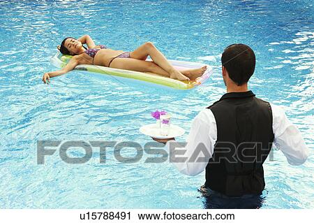 Stock Image - Waiter serving drinks to girl in a pool. Fotosearch