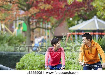 Stock Image - Woman and man cycling through the park. Fotosearch