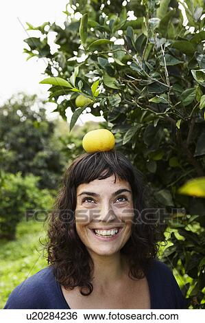 Stock Photograph - Woman balancing mandarin on her head. Fotosearch