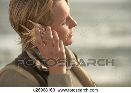 Stock Image - Woman by sea, listening in seashell. Fotosearch