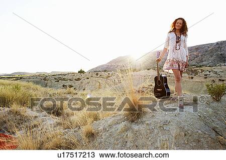 Stock Image - Woman carrying guitar at sunset. Fotosearch