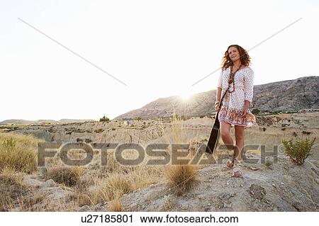Stock Image - Woman carrying guitar at sunset. Fotosearch