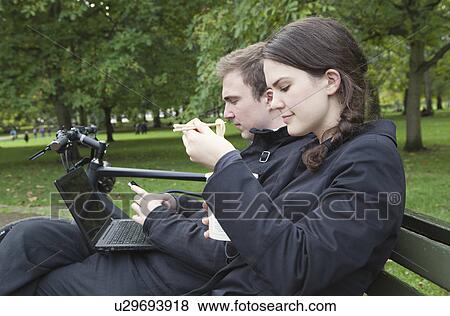 Stock Photo - Woman eating noodles on park bench. Fotosearch