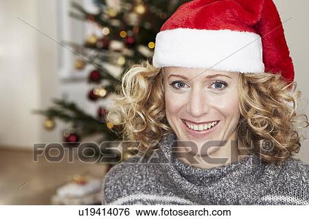 Stock Photograph - Woman in front of xmas tree wearing hat. Fotosearch