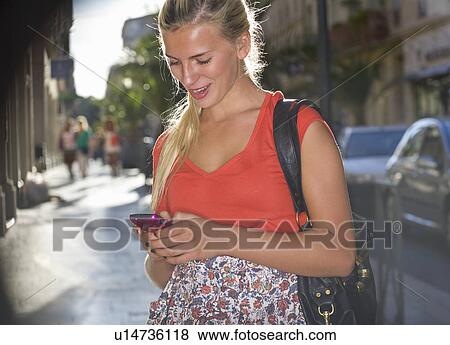 Stock Photo - Woman in street sends text on phone. Fotosearch