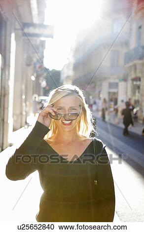 Stock Image - Woman looks over sunglasses in street. Fotosearch