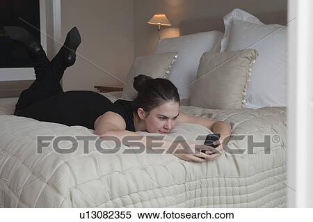 Woman lying on bed reading text message View Large Photo Image Stock Photography - Woman lying on bed reading text message. Fotosearch