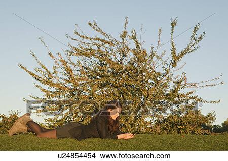 Picture - Woman lying on grass sending text. Fotosearch