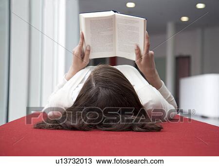 Stock Image - Woman lying on her back reading a book. Fotosearch